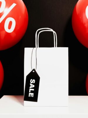 White shopping bag with sale tag surrounded by red balloons displaying percentage signs.